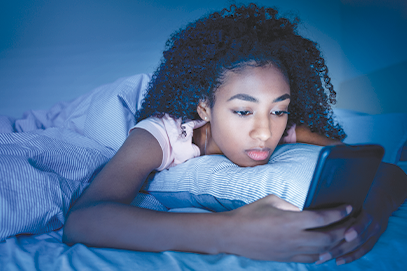 teen girl lying in bed at night looking at smart phone